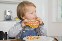 Cute female toddler eating cake at kitchen table — Stock Photo