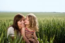 Child kissing mother in wheat-field — Stock Photo