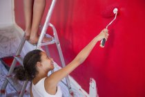 Niña y madre pintando pared roja con rodillo de pintura - foto de stock