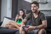 Young couple on sofa using smartphone and gaming control — Stock Photo