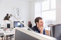 Mittlerer erwachsener Mann im Büro mit Computerhand am Kinn — Stockfoto