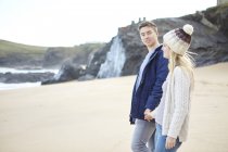 Молодая пара, прогуливающаяся рука об руку на пляже, Константин Бей, Корнуолл, Великобритания — стоковое фото