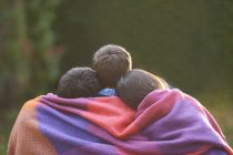 Братья и сестры, завернутые в одеяло в саду — стоковое фото