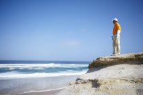 Low angle view of golfer standing on cliff overlooking ocean looking away — Stock Photo