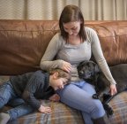Mother and son relaxing on sofa at home with pet labrador — Stock Photo