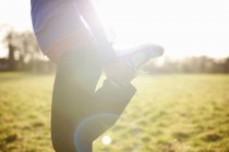 Cropped view of mature female runner stretching leg in field — Stock Photo