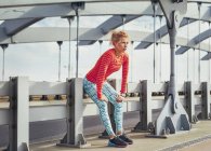 Молодая бегунья отдыхает на городском пешеходном мосту — стоковое фото