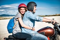 Mid adult couple riding motorcycle on arid plain, Cagliari, Sardegna, Italia — Foto stock