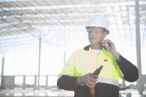 Builder with electric drill inserting earplugs on construction site — Stock Photo