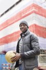 Ritratto di giovane uomo sorridente sulla strada che tiene il pallone da calcio — Foto stock