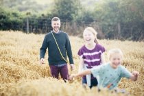 Pai com duas meninas correndo pelo campo — Fotografia de Stock