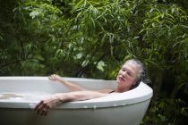Зрелая женщина отдыхает в ванной с пеной в саду на эко-ретрите — стоковое фото