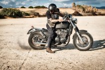 Homme adulte mature tournant roue de moto sur plaine aride, Cagliari, Sardaigne, Italie — Photo de stock