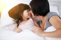 Jovem mãe chinesa e filha deitada na cama juntos em casa — Fotografia de Stock