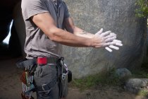 Plan recadré de jeune grimpeur masculin frottant de la craie sportive sur les mains — Photo de stock