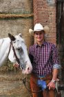Retrato de un joven en traje de vaquero con caballo fuera del establo - foto de stock