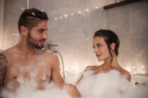 Jovem casal olhando um para o outro no banho de bolhas — Fotografia de Stock