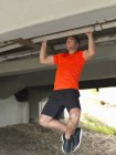 Junger Mann macht Klimmzüge unter Brücke — Stockfoto