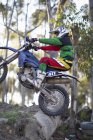 Young male motocross racer riding up over logs on forest track — Stock Photo