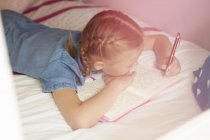 Visão de alto ângulo da menina deitada na cama e escrevendo no caderno — Fotografia de Stock