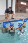 Quatro alunas jogadoras de polo aquático ouvindo professor junto à piscina — Fotografia de Stock