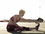 Молодая женщина дотрагивается до пальцев ног во время тренировки на парковке — стоковое фото