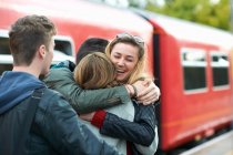 Grupo de amigos abrazándose en la estación de tren, sonriendo - foto de stock