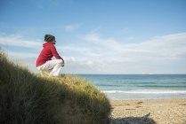 Mature woman crouching and gazing at sea water, Camaret-sur-mer, Brittany, France — Stock Photo