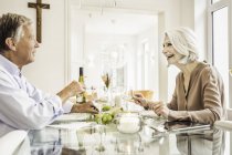 Seniorenpaar sitzt zusammen am Esstisch, von Angesicht zu Angesicht lächelnd — Stockfoto