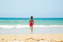 Rear view of boy in sea looking out towards horizon, Cadiz, Spain — стоковое фото