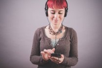 Retrato de estudio de mujer joven con pelo corto rosa eligiendo música en el teléfono inteligente - foto de stock