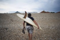Вид сзади серфера, несущего доску для серфинга на пляже — стоковое фото