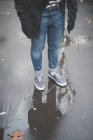 Обрізане зображення молодої стильної жінки в джинсах на мокрій асфальті — стокове фото