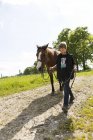 Мальчик ведет лошадь по грунтовой дороге — стоковое фото
