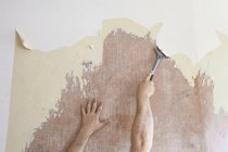 Mature man using scraper to scrape off old wallpaper — Stock Photo
