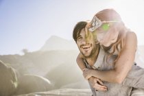 Homem na frente de rochas dando mulher piggyback sorrindo — Fotografia de Stock