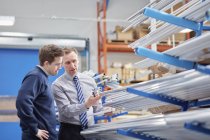 Manager and factory worker checking shelves of metal rods in roller blind factory — Stock Photo