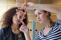 Two young female designers looking at handmade model in creative office — Stock Photo