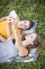 Молода пара лежить на траві в полі, беручи автопортрет за допомогою смартфона — стокове фото