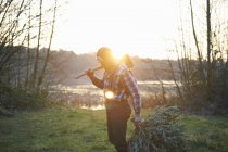 Woodsman with axe over his shoulder in forest at sunset — Stock Photo