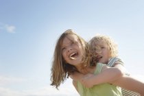 Low angle view of girl giving sister piggy back at coast — Stock Photo