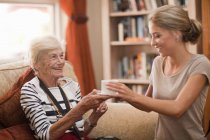 Care assistant handing coffee cup to senior woman — Stock Photo