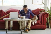 Mid adult man writing address on parcels whilst petting dog in picture framers — Stock Photo