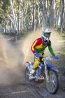 Young male motocross racer splashing through forest track — Stock Photo
