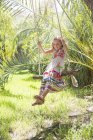 Girl sitting swinging on tree swing in garden — Stock Photo