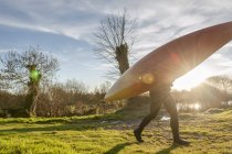Side view of woman carrying canoe in field — Stock Photo