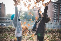 Two young women throwing autumn leaves in park — Stock Photo