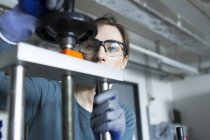 Woman in workshop wearing safety goggles adjusting machine — Stock Photo