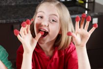 Chica con frambuesas en los dedos - foto de stock