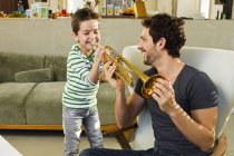 Pai encorajando pequeno filho tocando trompete — Fotografia de Stock